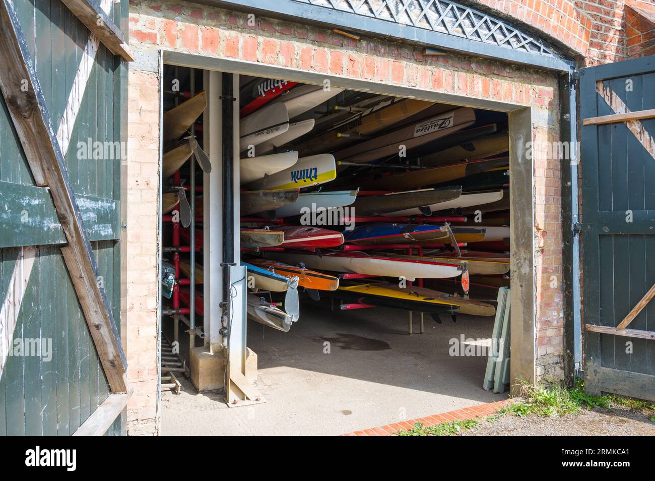 Viewed through open doors, a variety of canoes, kayaks and rowing sculls stored in the Richmond Canoe Club boathouse. Richmond, London, England, UK Stock Photo
