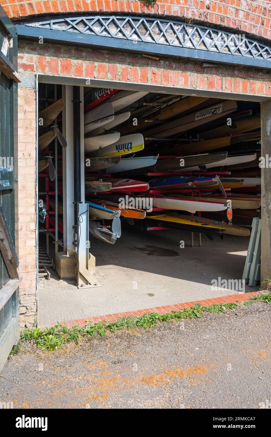 Viewed through open doors, a variety of canoes, kayaks and rowing sculls stored in the Richmond Canoe Club boathouse. Richmond, London, England, UK Stock Photo