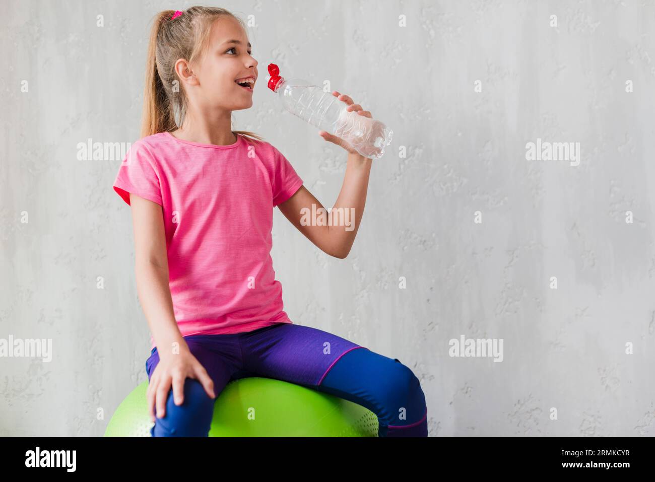 Smiling girl sitting green pilates ball drinking water from bottle