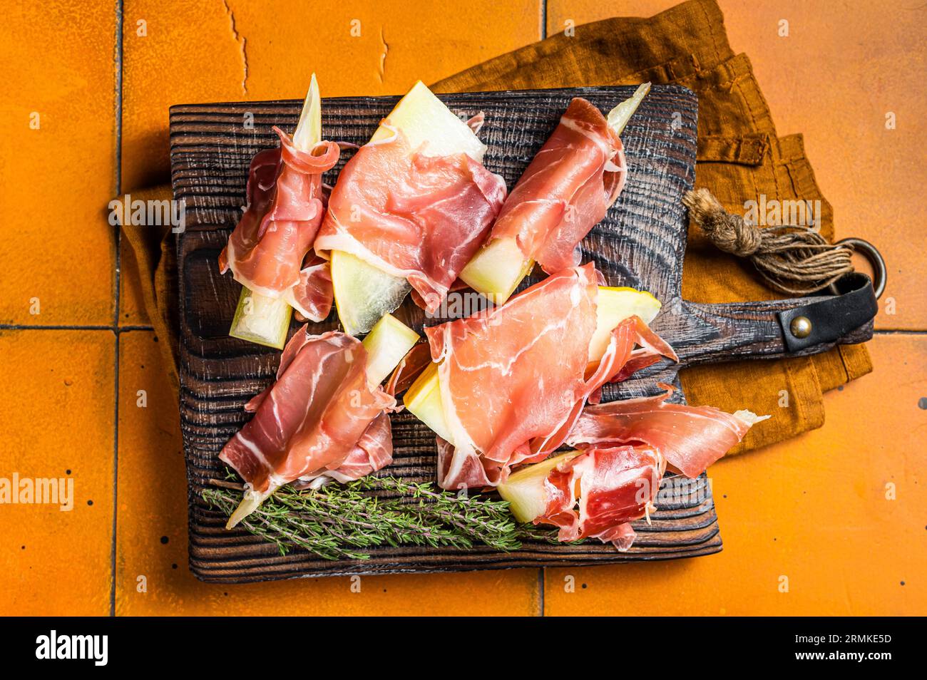 Prosciutto ham with slices of melon and fresh thyme. Orange background