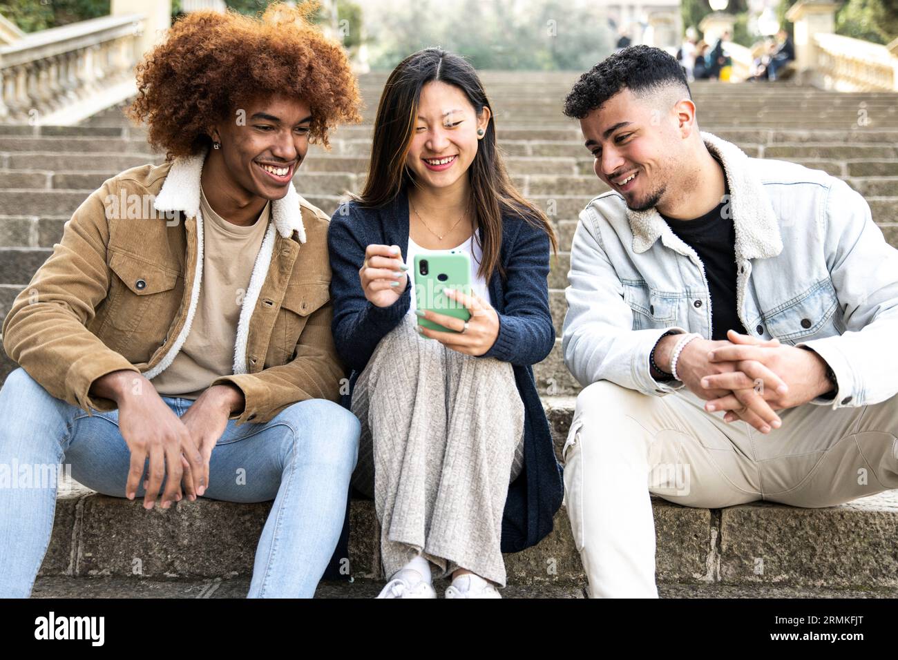 Three young diverse people looking at a smartphone sitting on the ...