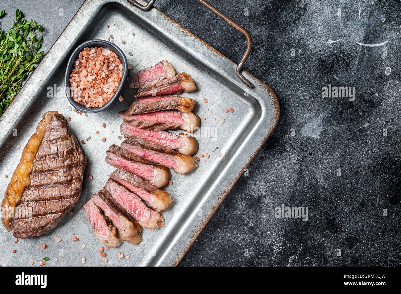 Grilled and sliced brazilian Picanha steak, cup rump beef meat steak on a steel serving tray with herbs. Black background. Top view. Copy space. Stock Photo