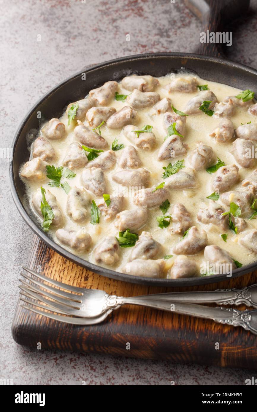 Delicious chicken hearts in garlic cream sauce close-up in a plate on the table. Vertical Stock Photo