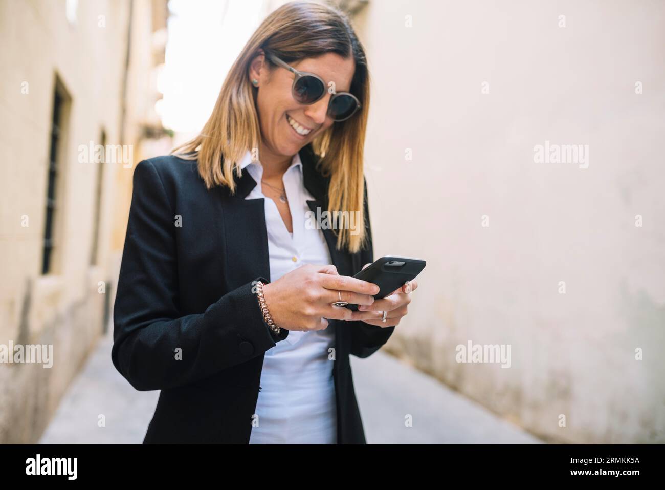 Smiling elegant young woman using smartphone buildings street Stock Photo