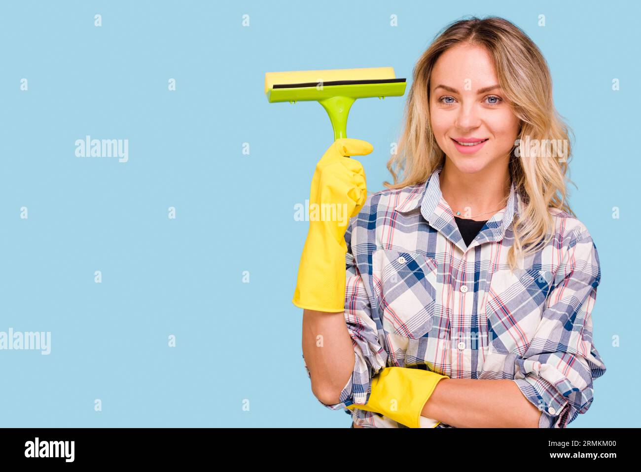 Young smiling woman holding plastic wiper looking camera against blue background Stock Photo