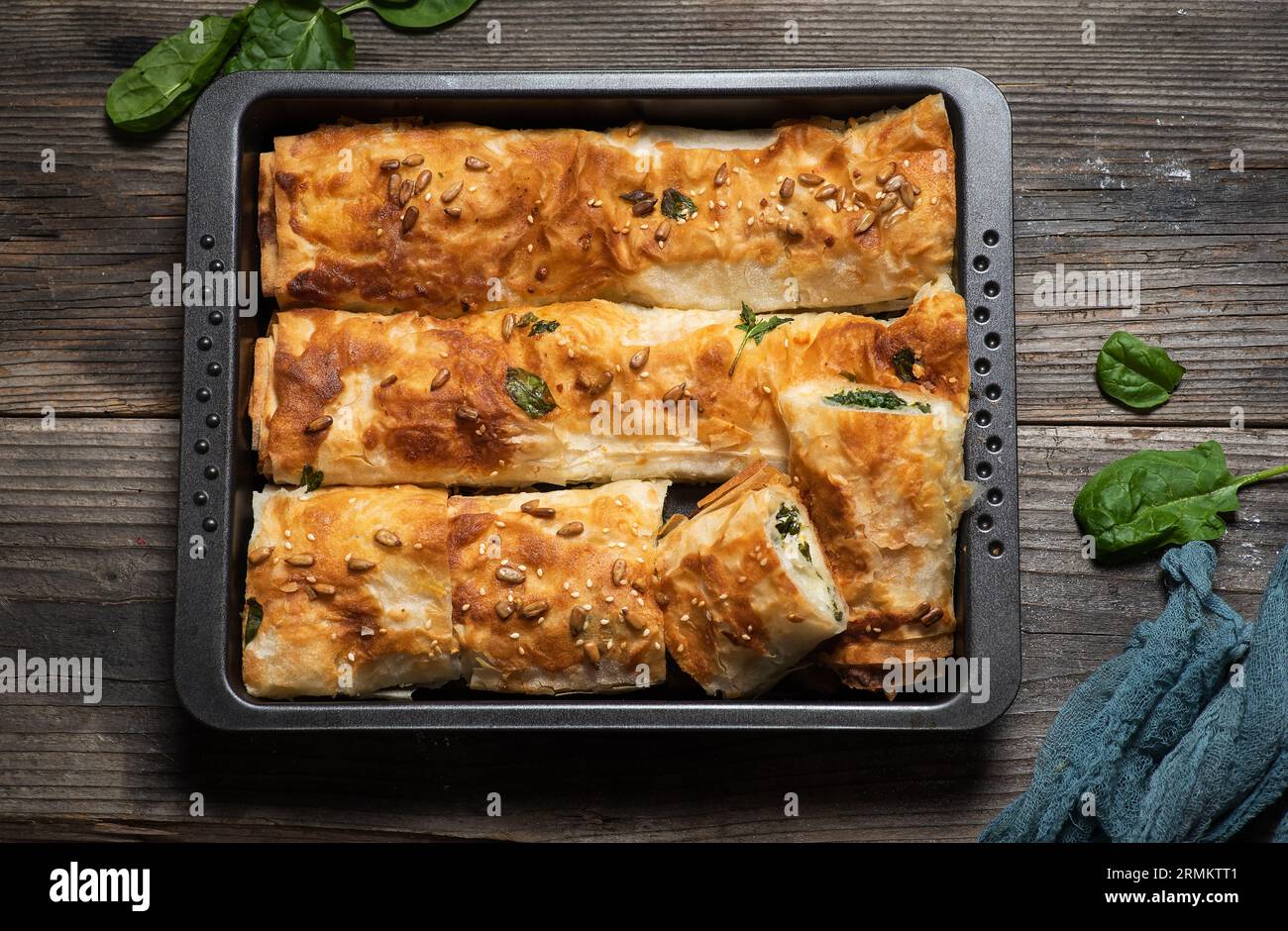 Freshly baked homemade rolled pie with spinach in a baking tray on a wooden background. Top view. Stock Photo
