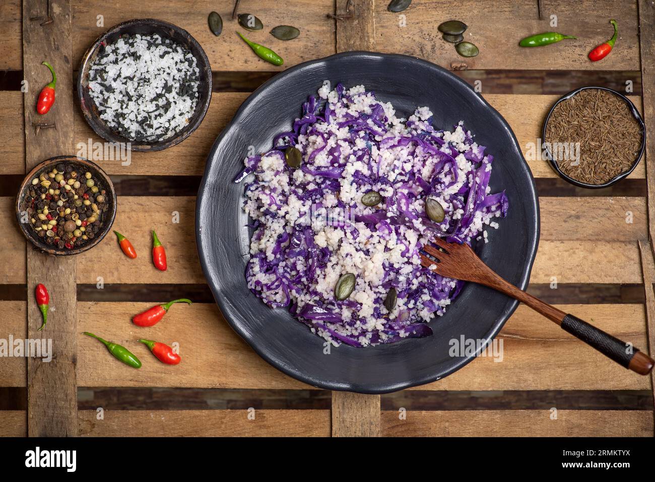 Couscous with red cabbage, fresh and dry spices in a food preparation bowl on a rustic wooden background. Top view Stock Photo