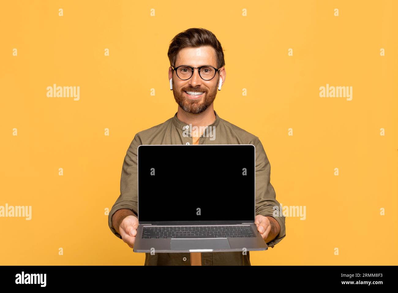 Positive middle aged man showing modern laptop with black empty screen, mockup for online offer, app, website advert Stock Photo