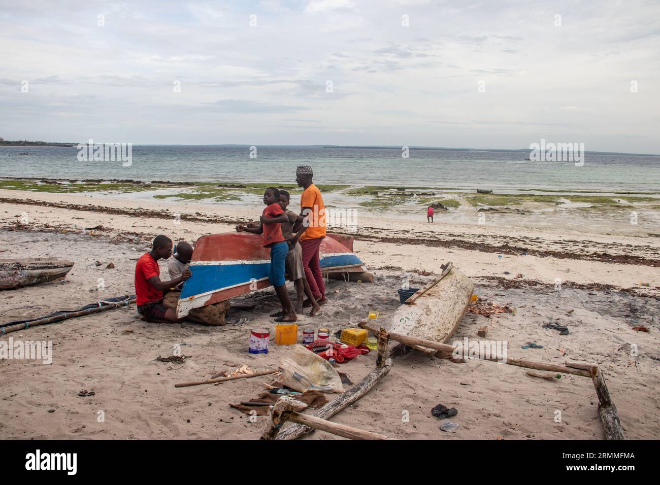 Group of African people fixing and maintaining fisherman's colorful wooden boat, at the shore of Indian Ocean. Bunch of curious kids wondering around Stock Photo