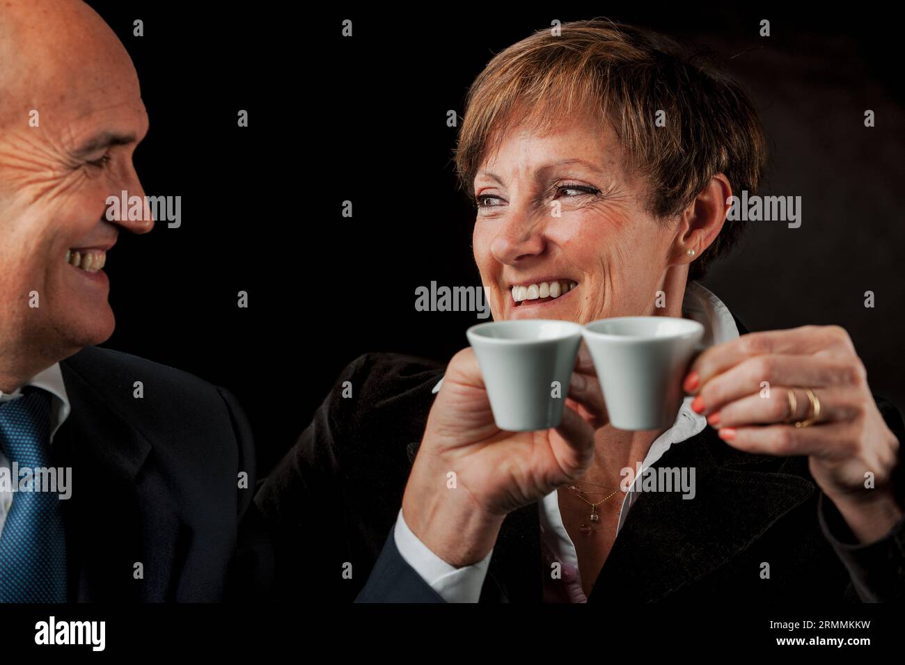 Two elderly well-to-do individuals, enjoying authentic Italian espresso while touring Europe, are portrayed against a black backdrop. The bald gentlem Stock Photo
