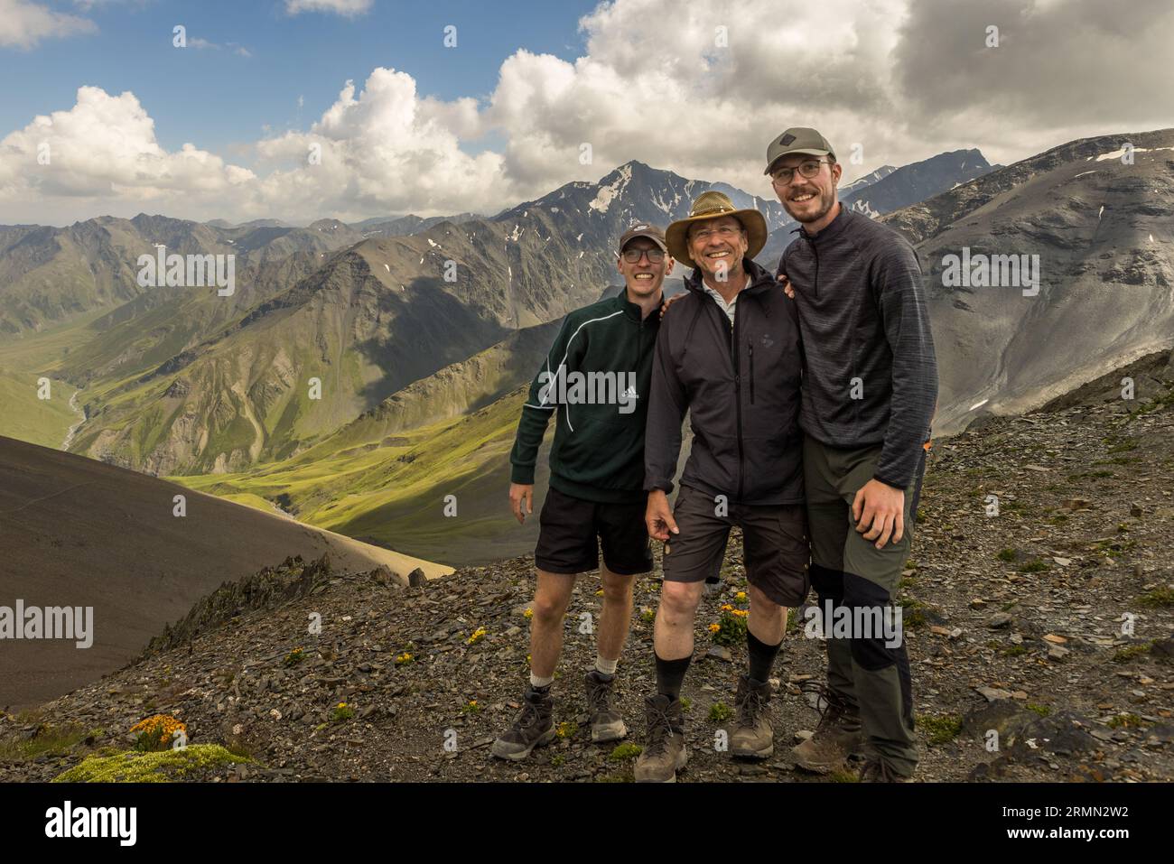 A group of three trekkers on the Atsunta Pass (3,431 m), with the Caucasus ridge and the steep-sided valley on the Khevsureti side in the background. The pass in the Greater Caucasus, Georgia, connects the provinces of Tusheti and Chewsureti and is only free of snow from July to September. Shavtskala, Akhmeta Municipality, Kakheti, 0900, Georgia Stock Photo