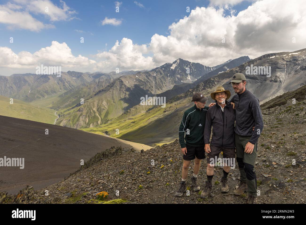 Three trekkers at the summit of the Atsunta Pass (3,431 m), looking out over the vast high valley on the Tusheti side and the Caucasus ridge. The pass is the highest point on a multi-day trek through north-eastern Georgia between Tusheti and Khevsureti. Shavtskala, Akhmeta Municipality, Kakheti, 0900, Georgia Stock Photo