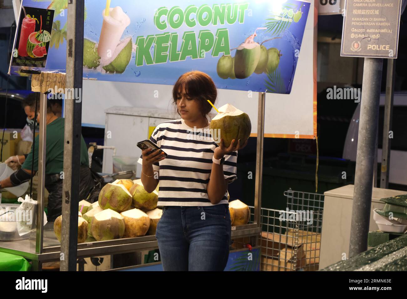 A woman looks at her phone while holding a coconut juice drink at a Deepawali night market in Singapore's Little India. 22/10/2022 Stock Photo