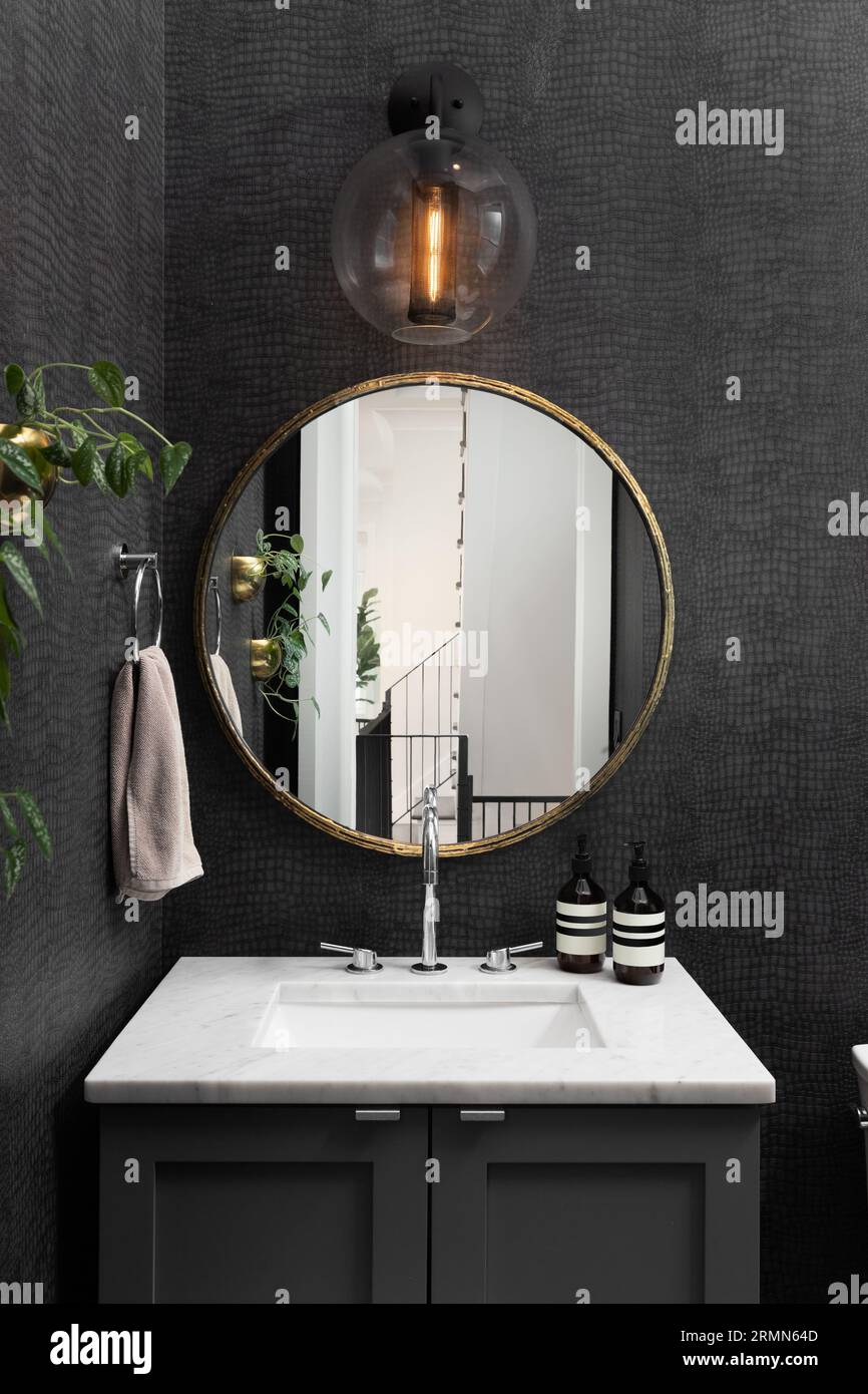 A bathroom with black snake skin wallpaper, circular gold mirror