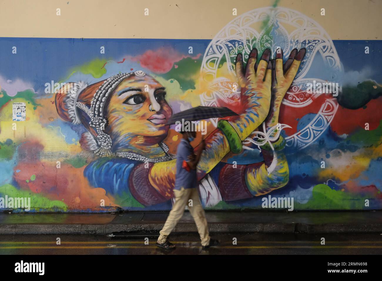 A man with an umbrella walks past Deepawali-themed street art in Singapore's bustling Little India area. 22/10/2022 Stock Photo