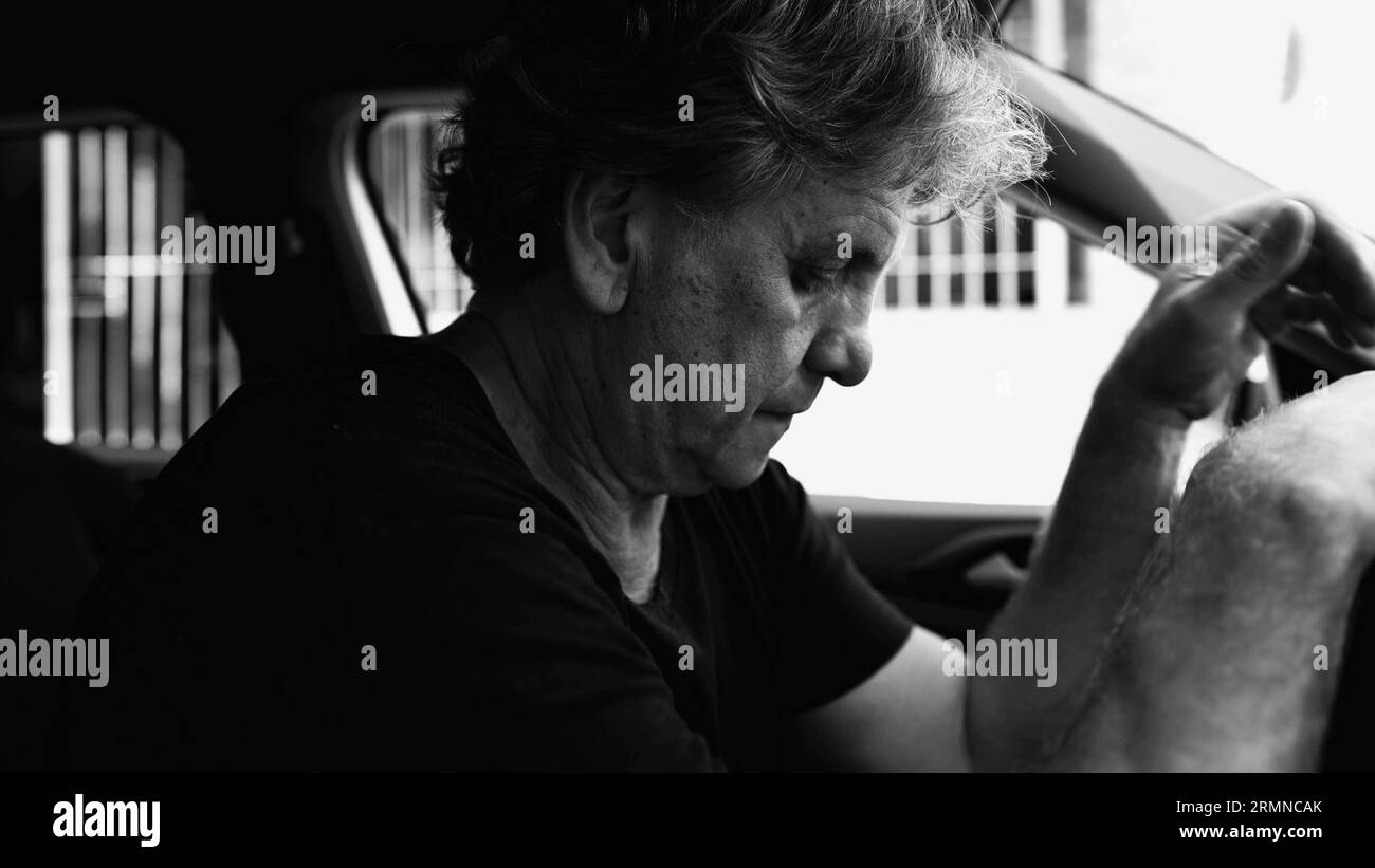 Senior Man Experiencing Sadness in Parked Car, Holding Steering Wheel, Struggling with Depression, dramatic black and white Stock Photo