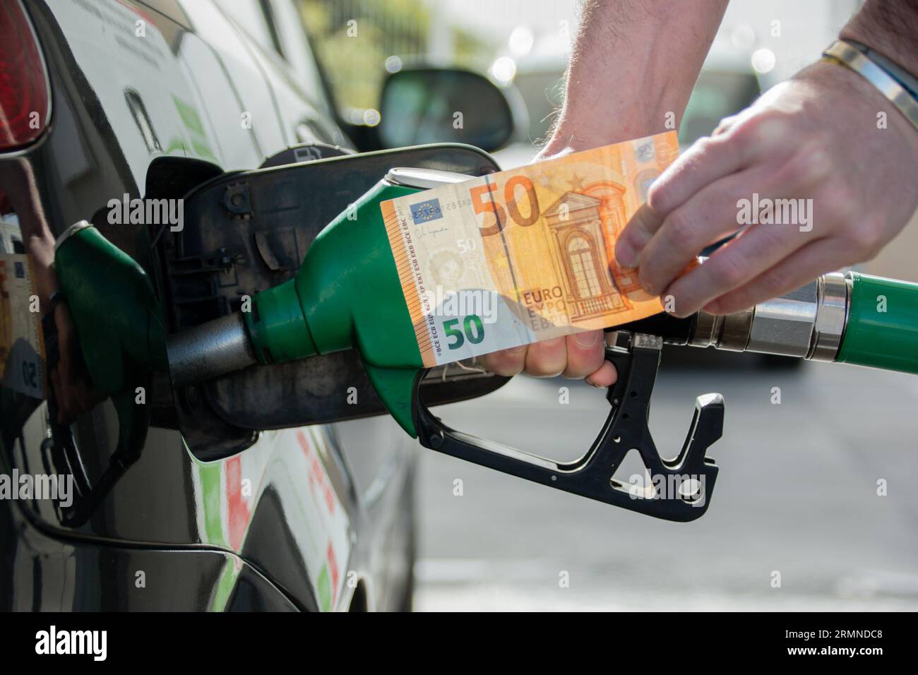 The hands of a man refueling his car holding a 50 euro banknote. Concept of rising cost of living Stock Photo