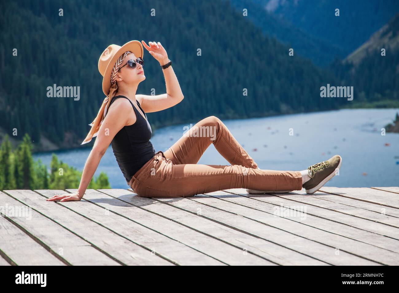 A young woman in safari style enjoys amazing nature at the Kolsai mountain lake, nature of Kazakhstan National Park, Central Asia Stock Photo