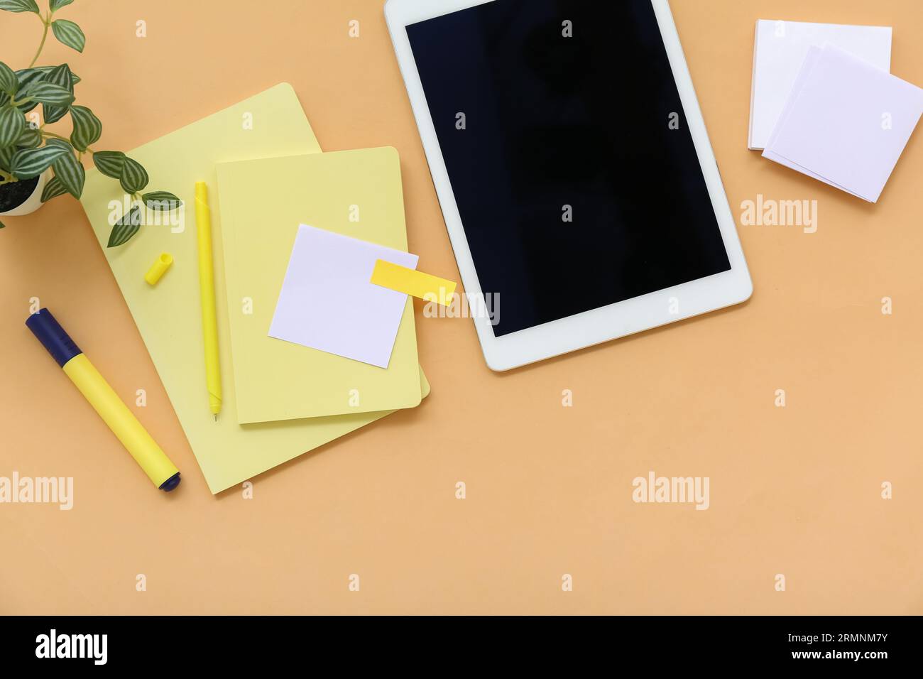 Tablet with notebooks and sticky notes on orange background Stock Photo
