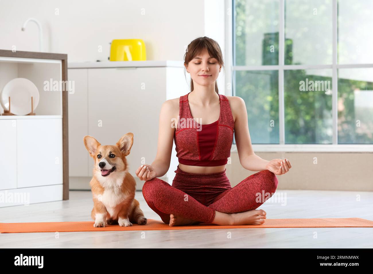 Sporty young woman meditating with cute Corgi dog on yoga mat in
