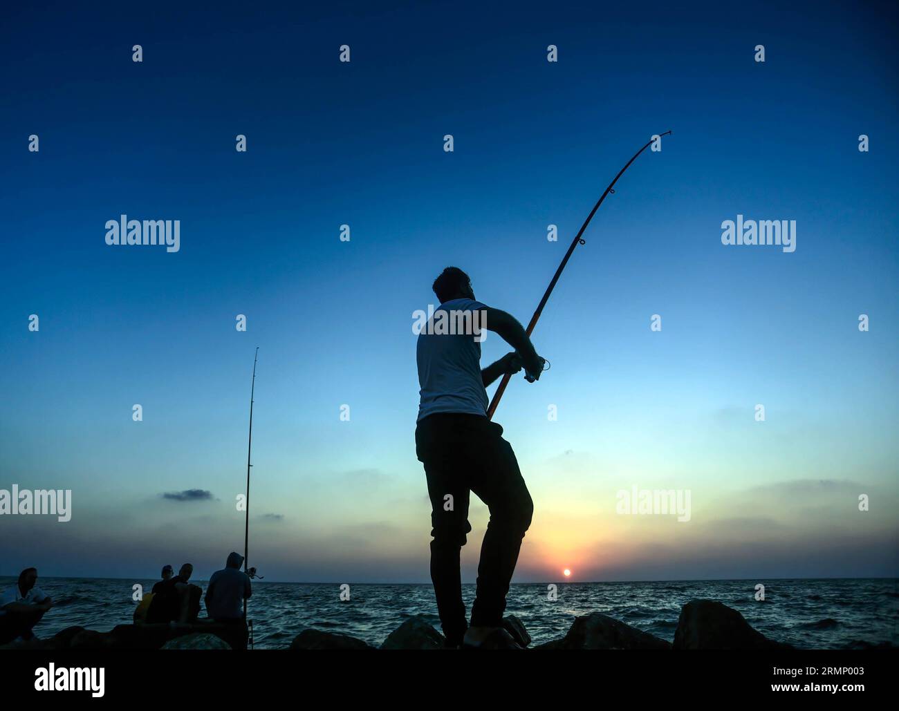Palestinian men use fishing rods to catch fish during sunset on