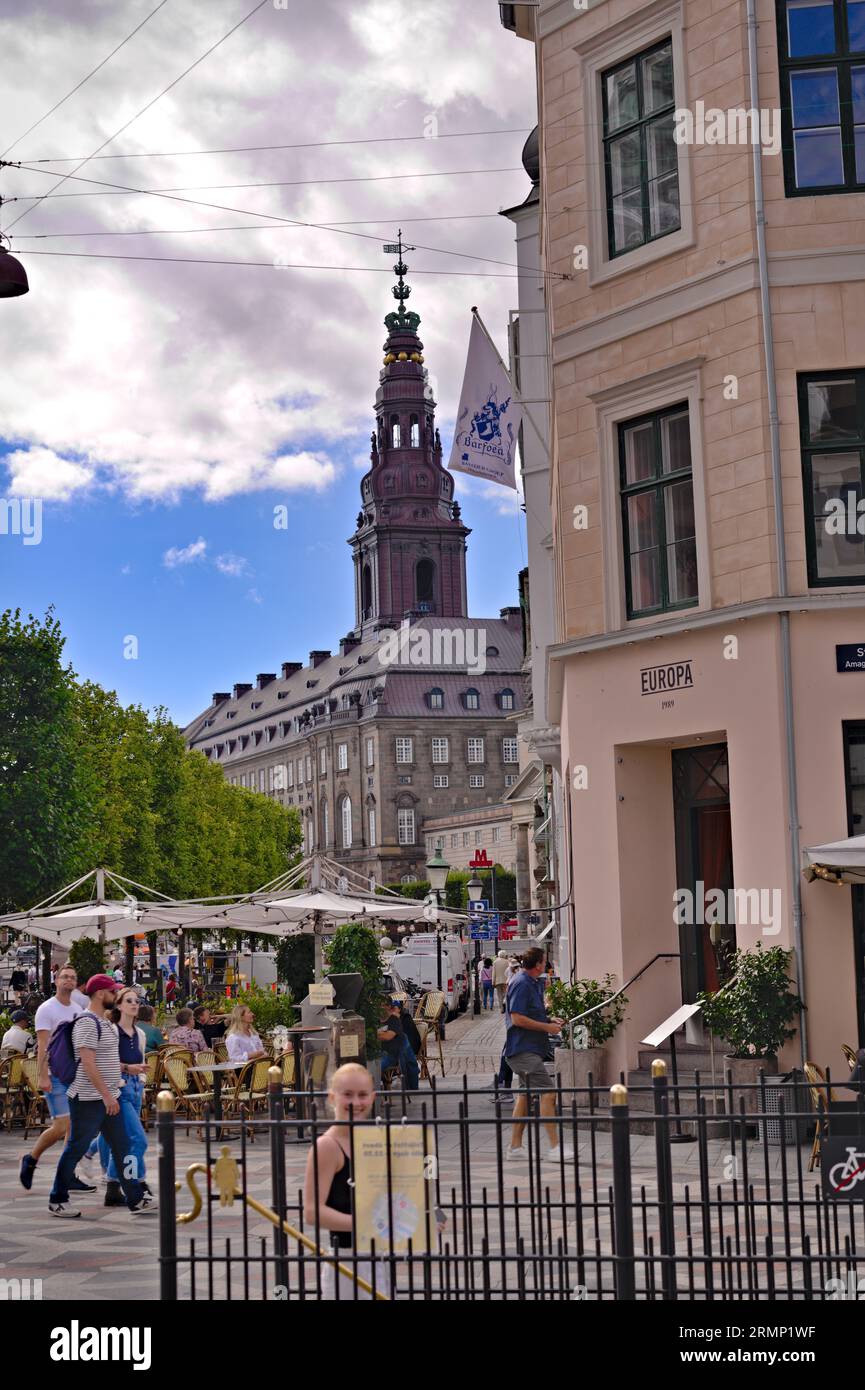 View of tourists shoppers walking on pedestrian street on Amagertorv square past a terrace and cafe.Tower of Christians borg Palace in the background Stock Photo