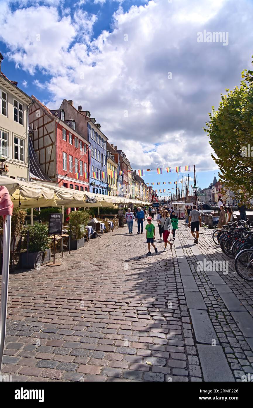 Diverse people walking through the Nyhavn canal tourist attraction of the capital with quaint colorful facade houses with LGBTQ+ flags in COPENHAGEN Stock Photo