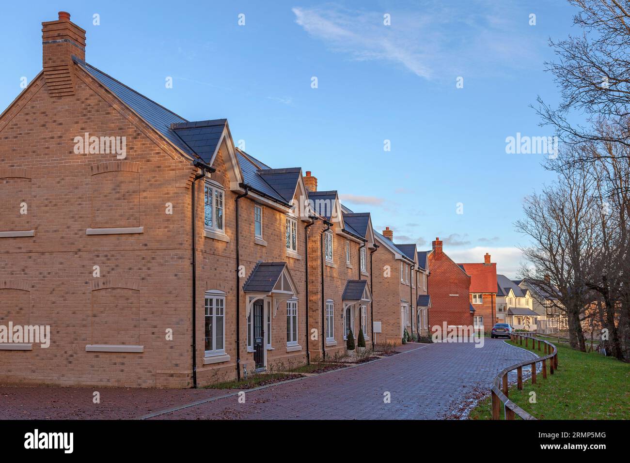 A new housing estate on a very early morning in December, as the dawning sunrise dapples its light through wood-side trees under the blue sky above. Stock Photo