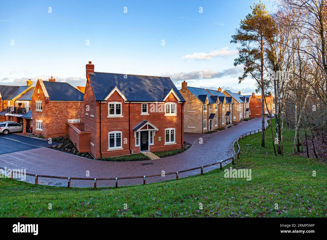 A new housing estate on a very early morning in December, as the dawning sunrise dapples its light through wood-side trees under the blue sky above. Stock Photo