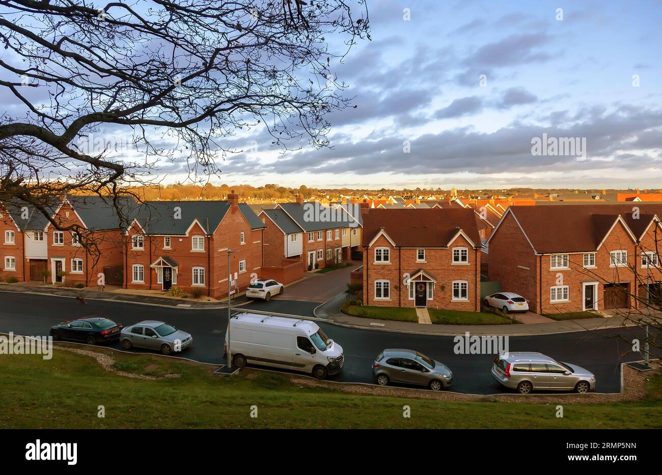A new housing estate on a very early morning in December, viewed as the dawning sunrise spreads its light across the rooftops under scudding clouds. Stock Photo