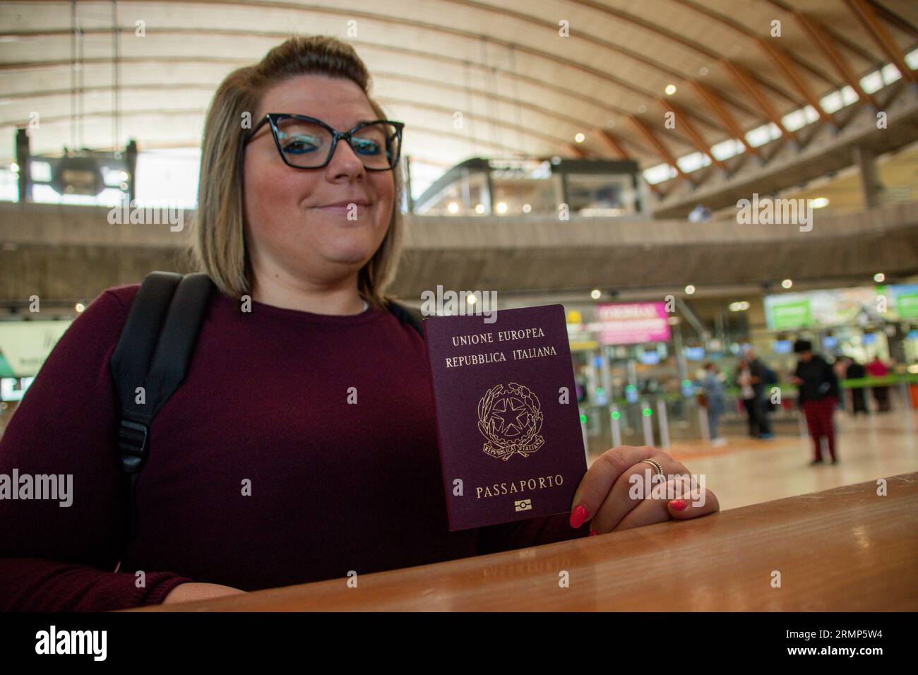 Smiling young Caucasian female traveler on departure at the airport. She shows the Italian passport Stock Photo