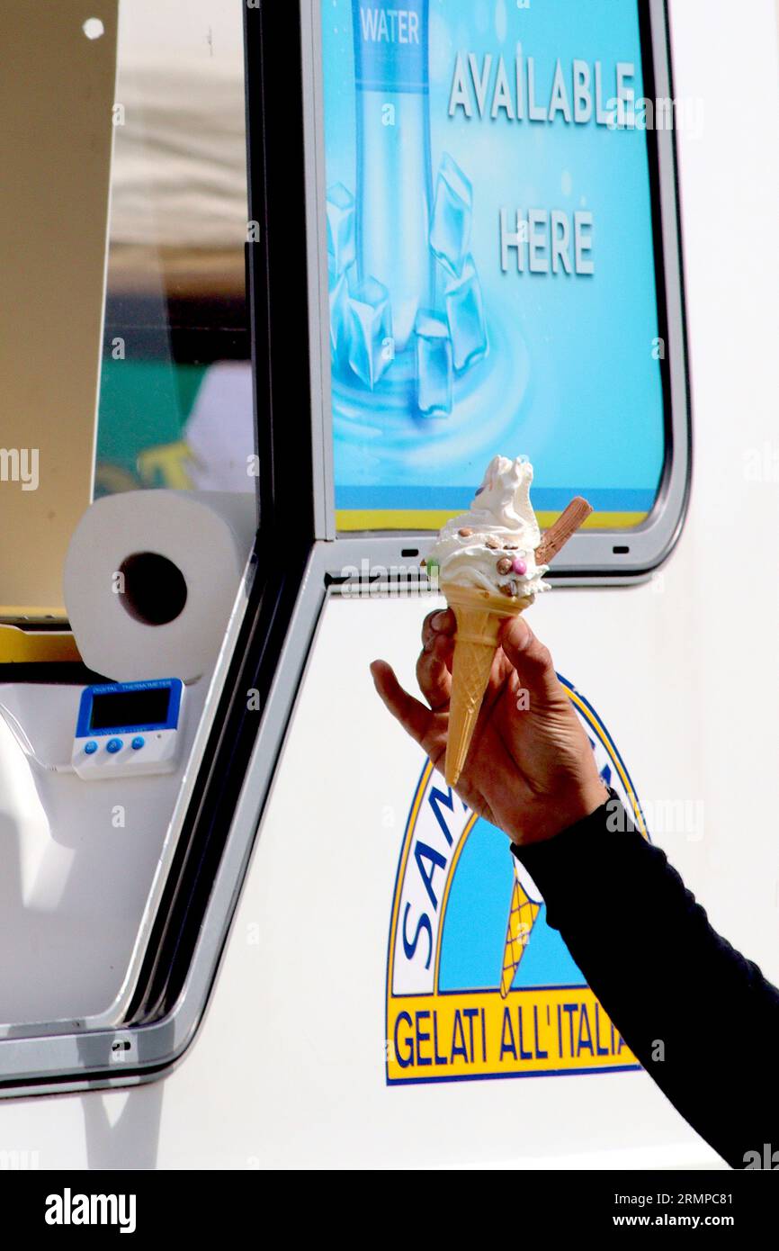 A customer takes a 99 Flake ice cream with added mini milk chocolate beans, from an ice cream van serving hatch, attending a food show, August 2023. Stock Photo