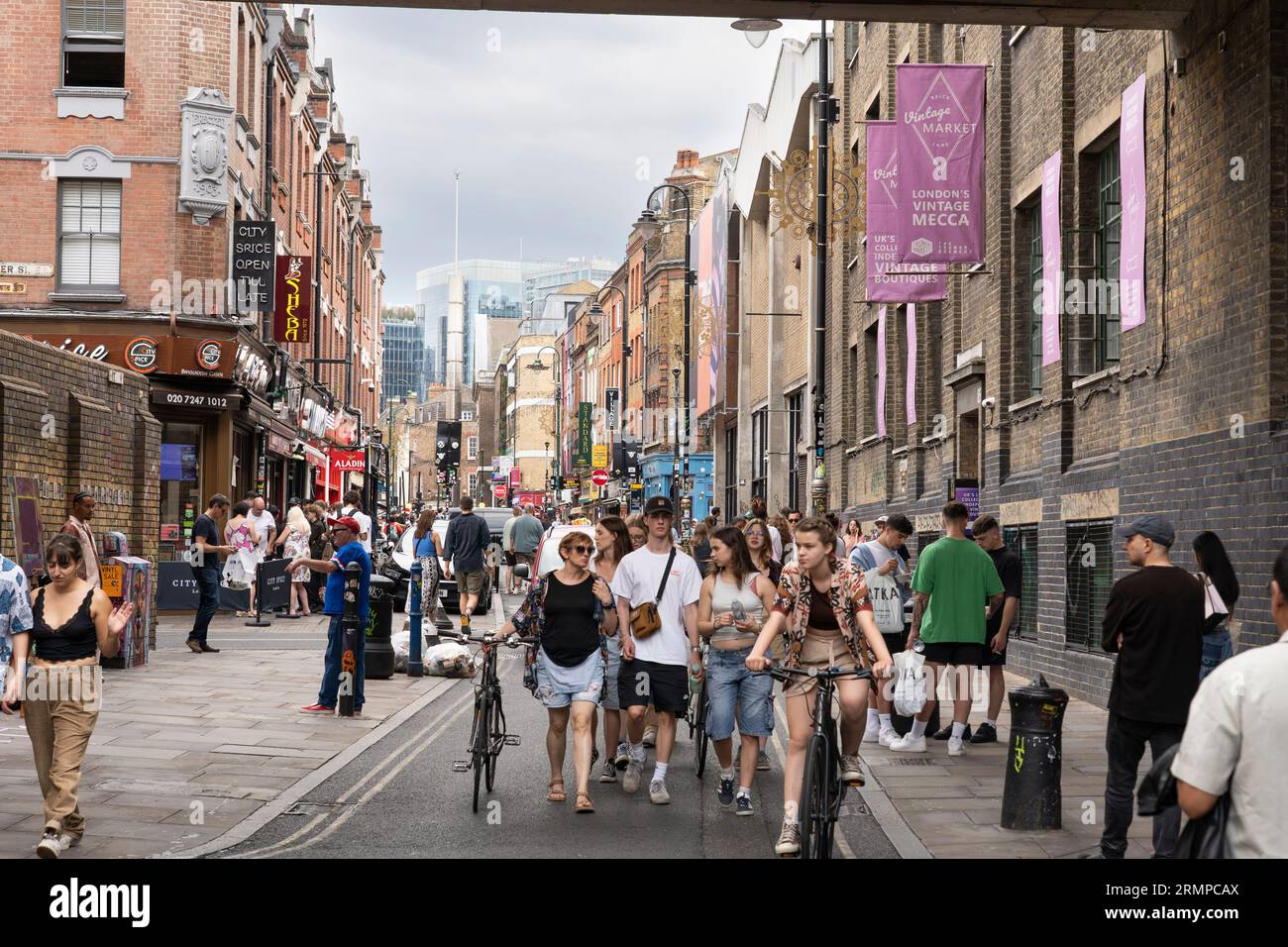 People walking and cycling along Brick Lane - a famous street in the East End of London and the heart of the country's Bangladeshi community. UK Stock Photo