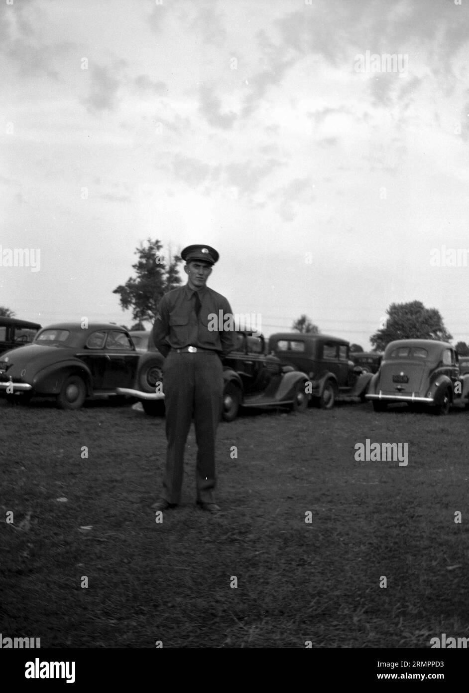 Soldier in uniform standing near cars. Members of the United States Army’s 114th infantry division train to fight against Germany in Europe during WWII. Stock Photo