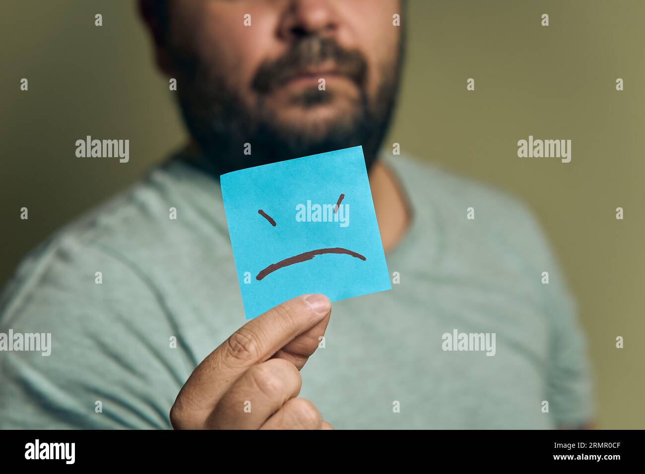 A bearded European man holds a orange sticker in front of him, with a sad smiley Stock Photo