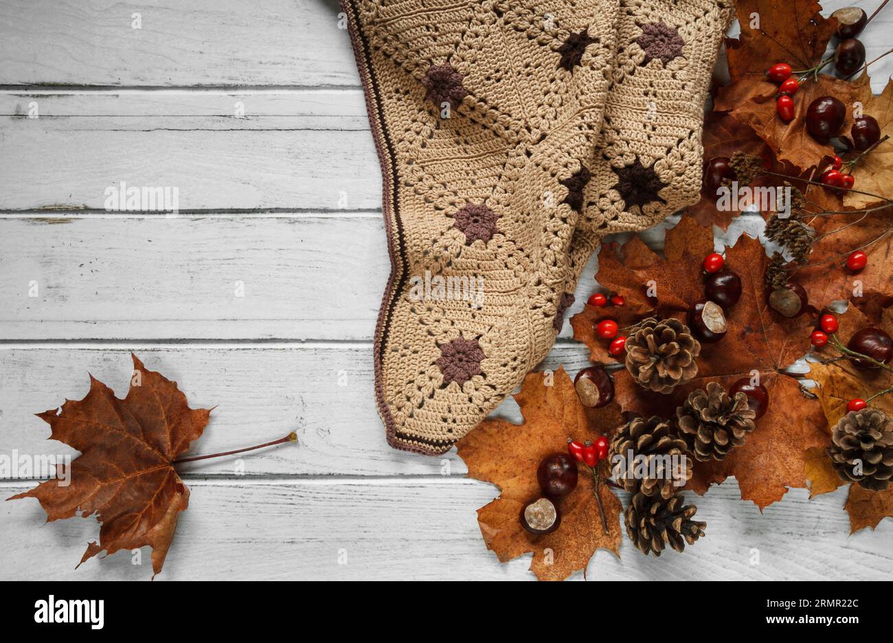 Warm, cosy handmade blanket, with autumn leaves, cones and chestnuts. Fall flat lay composition on white wooden table, with copy space. Stock Photo