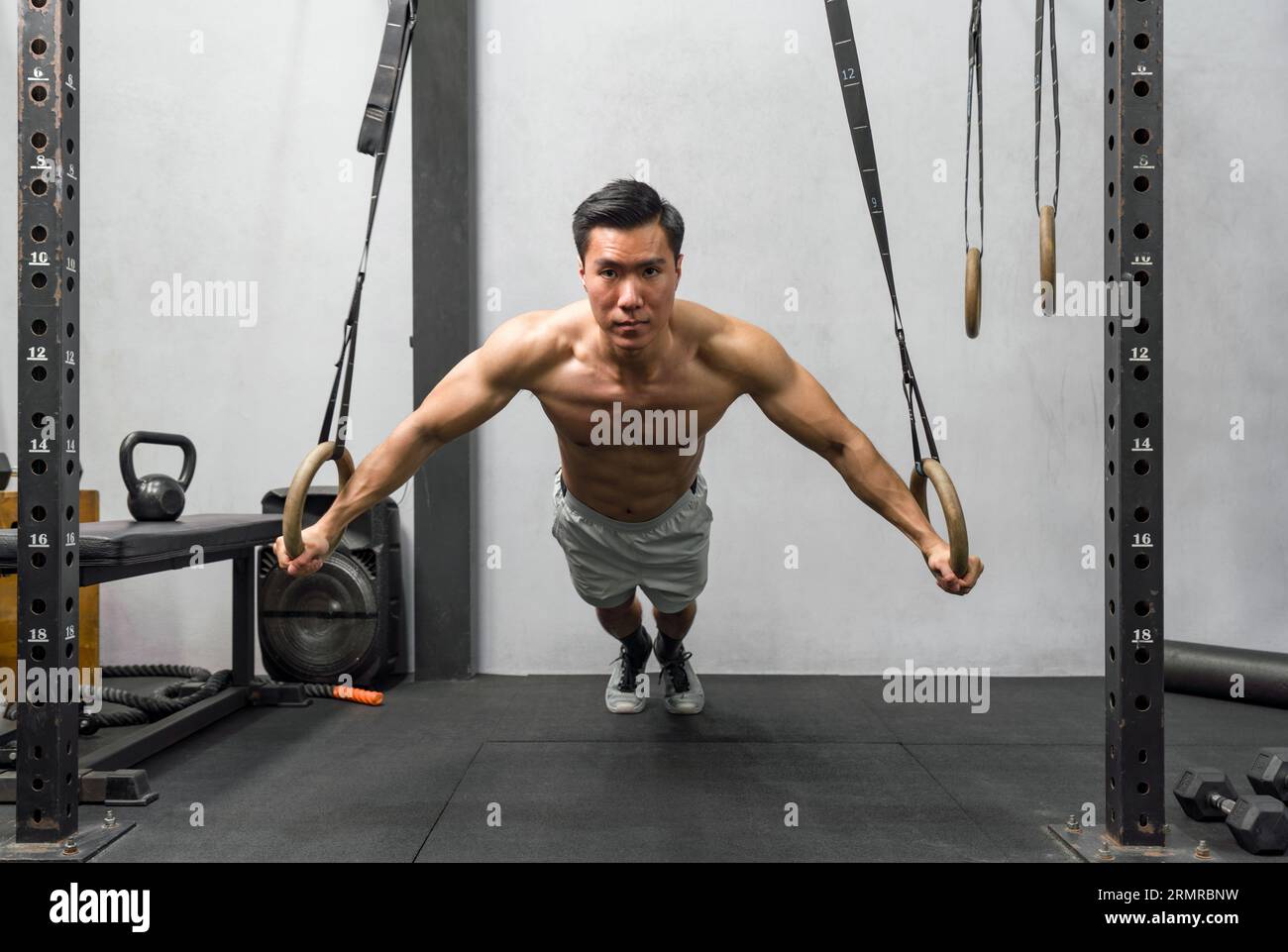 Athlete exercising on gymnastic rings in a well-equipped, modern gym. The man displays strength and determination, his muscles ripple with exertion. Stock Photo
