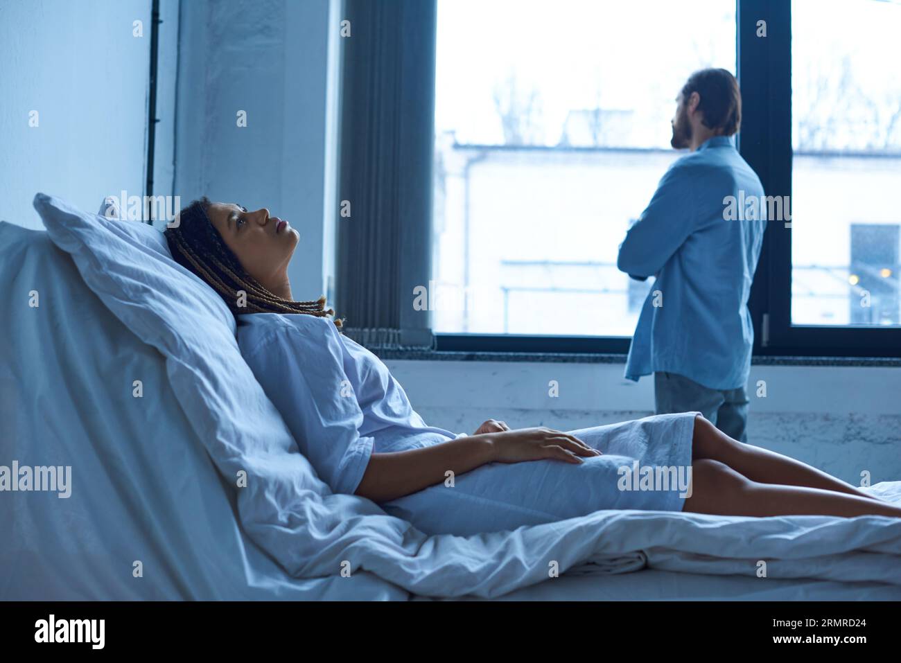 miscarriage concept, depressed african american woman grieving, lying in hospital bed near husband Stock Photo