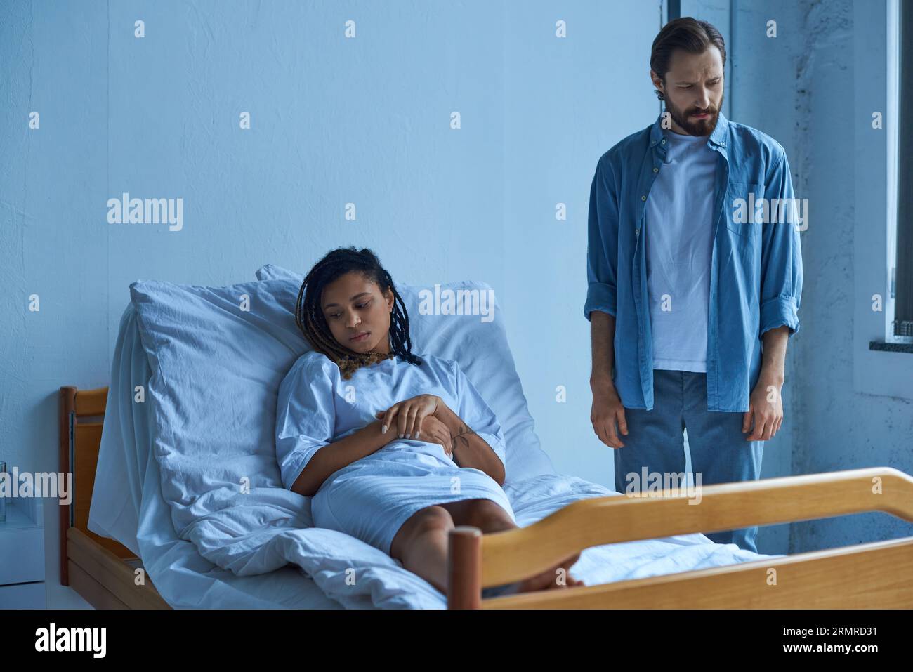 miscarriage concept, sad african american woman grieving, lying in hospital bed near husband, ward Stock Photo