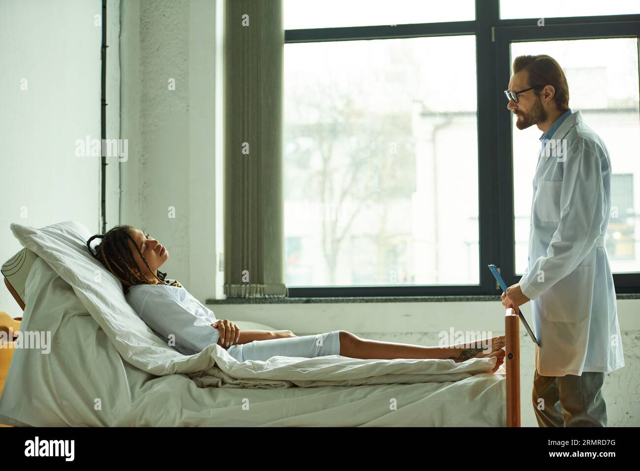 doctor standing with clipboard near african american woman, private ward, hospital, consultation Stock Photo