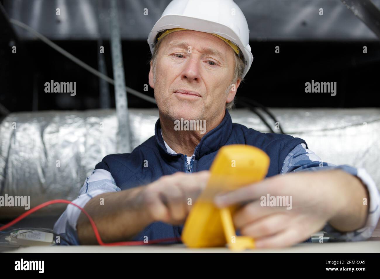 electrician measuring voltage of cable on ceiling indoors Stock Photo