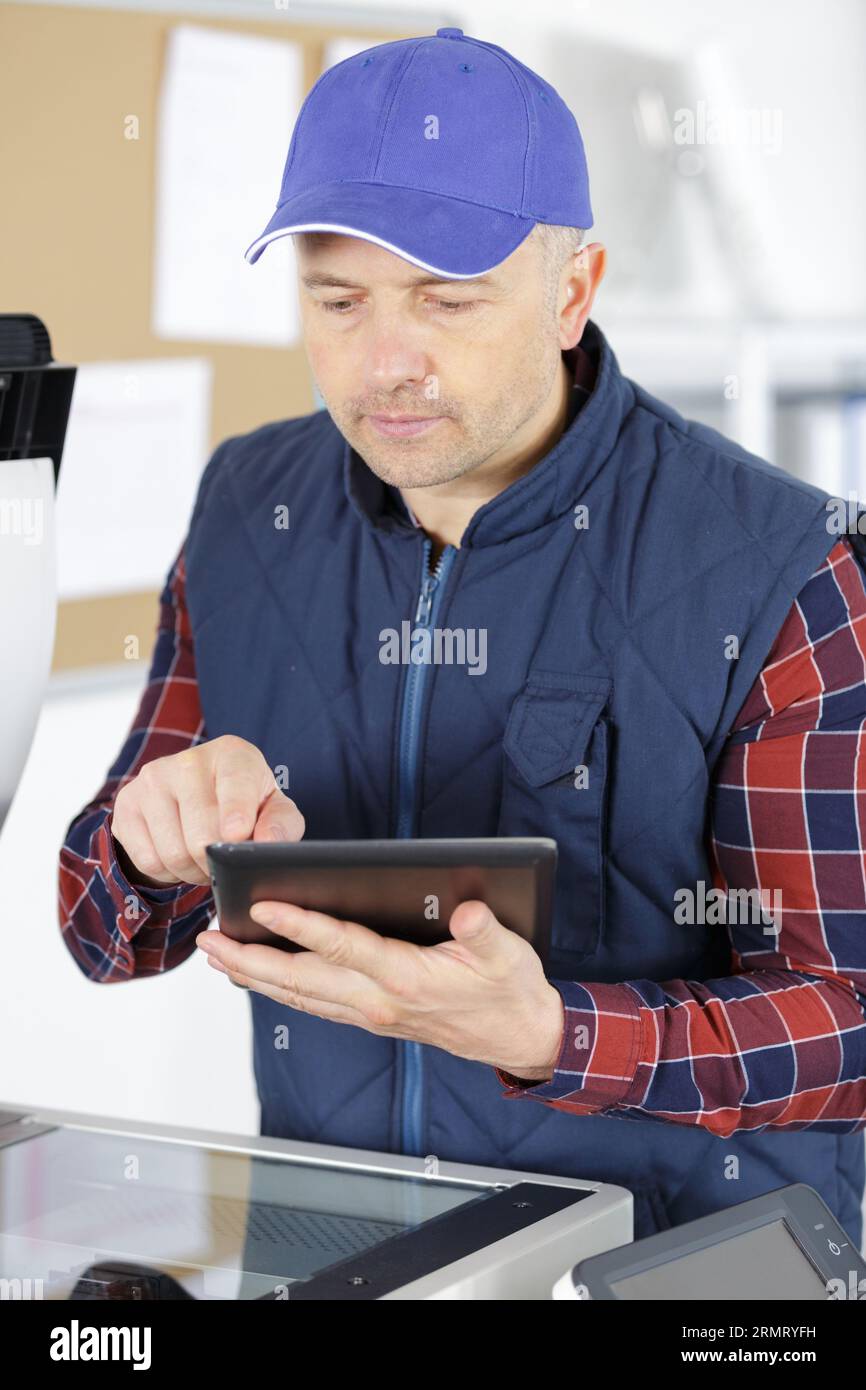 a technician using a tablet to fix a printer Stock Photo