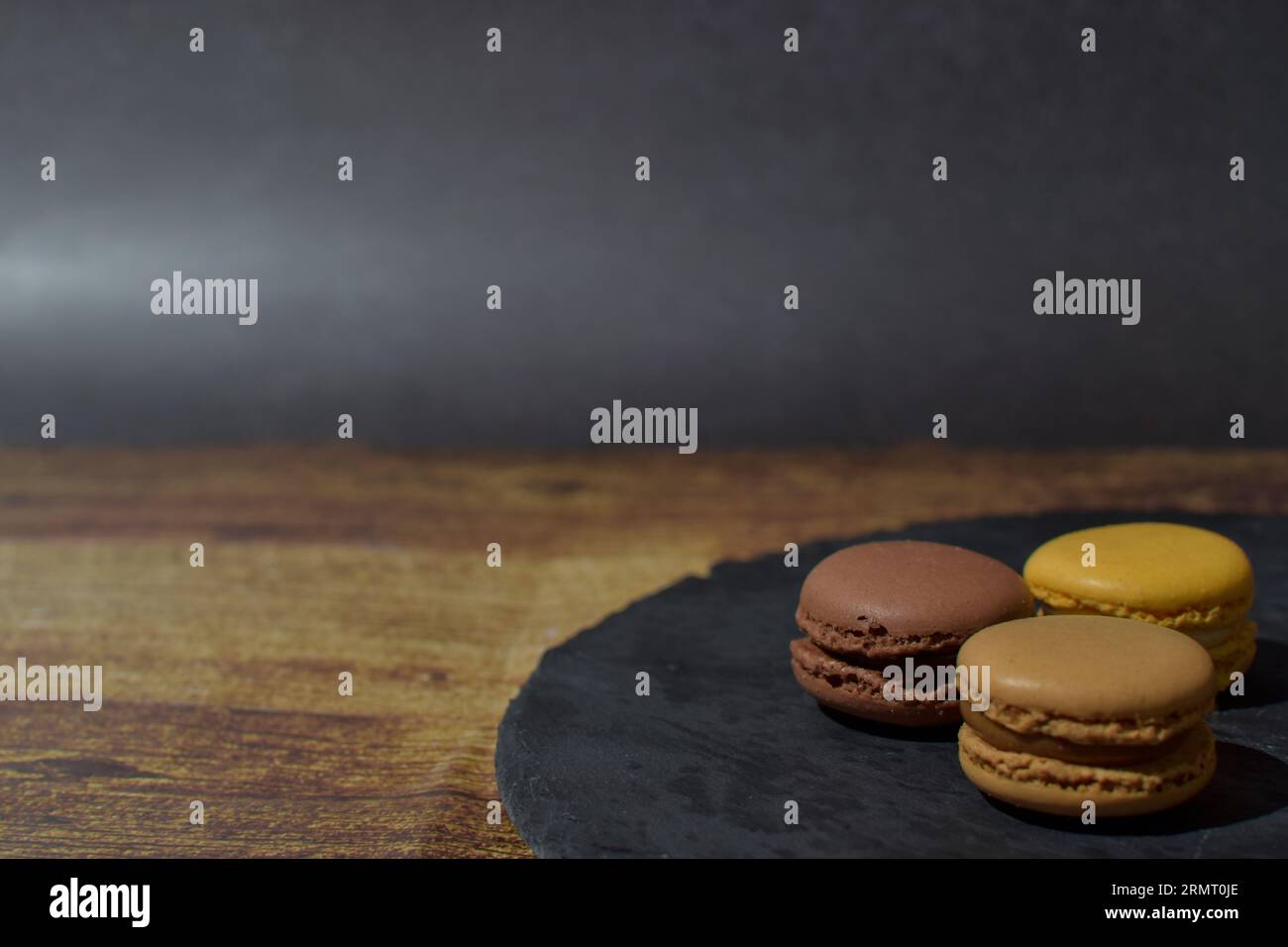 Macarons in brown and yellow tones, on a slate plate, on a wooden table Stock Photo