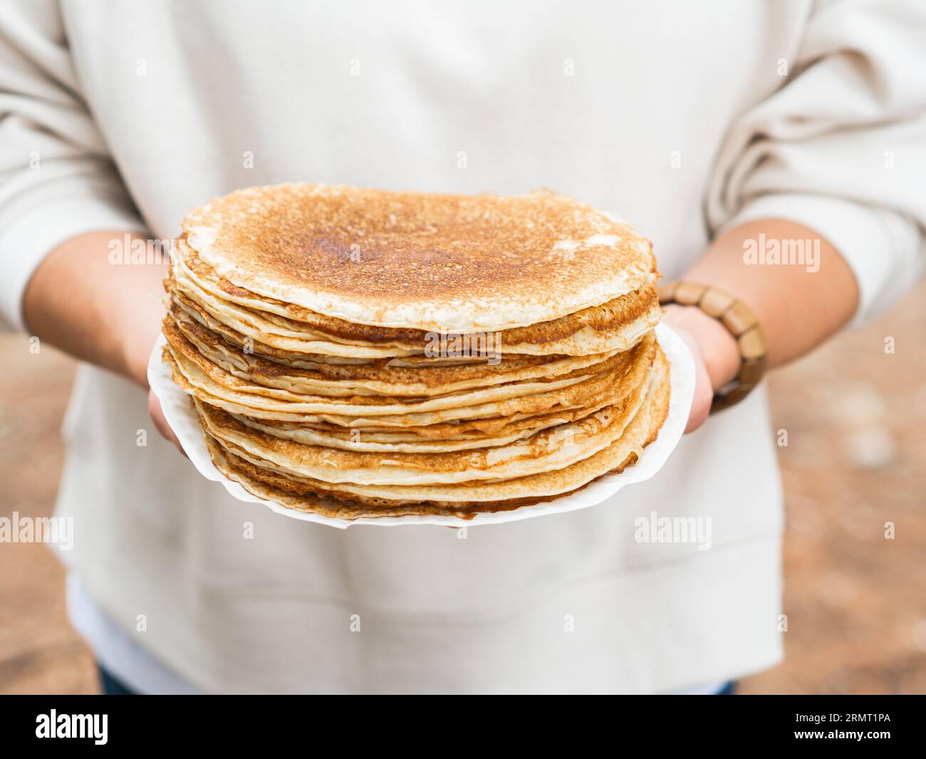 Women holding white plate with pile thin pancakes. Many pancakes are