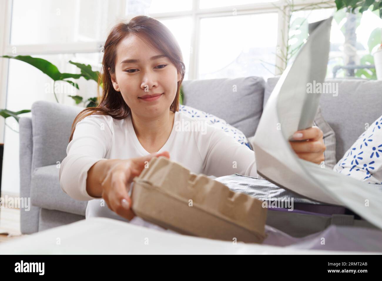 Asian female separate garbage at home. young woman sorting and recycling plastic, paper, aluminum can and food container to trash bins in living room Stock Photo