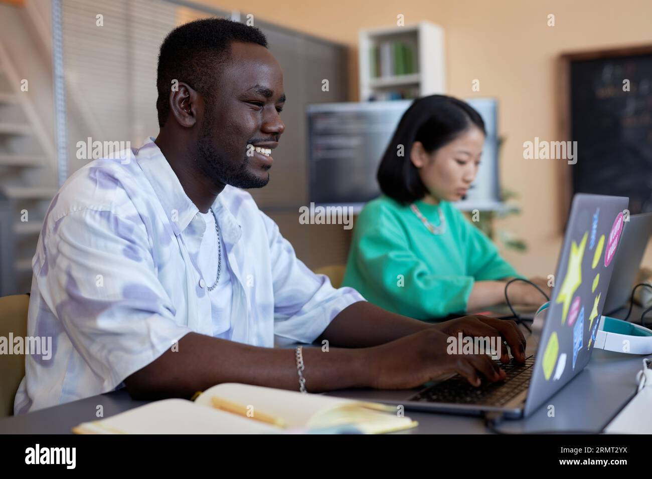 Smiling African American guy typing on laptop keyboard at informatics lesson while working over developing new software for decoding data Stock Photo