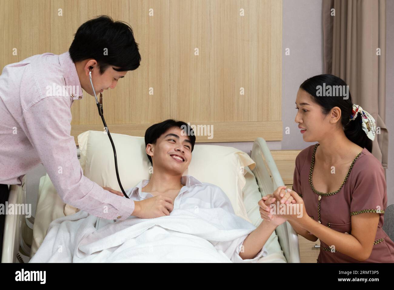 asian doctor using stethoscope listening heartbeat of patient and nurse writing health checklist at hospital. Recovery patient laying on bed after sur Stock Photo