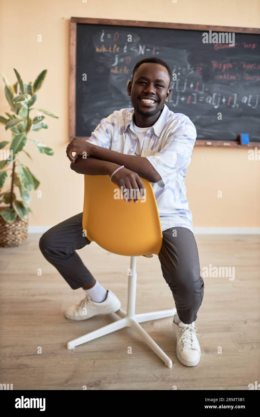 Young cheerful African American male student sitting on chair against ...