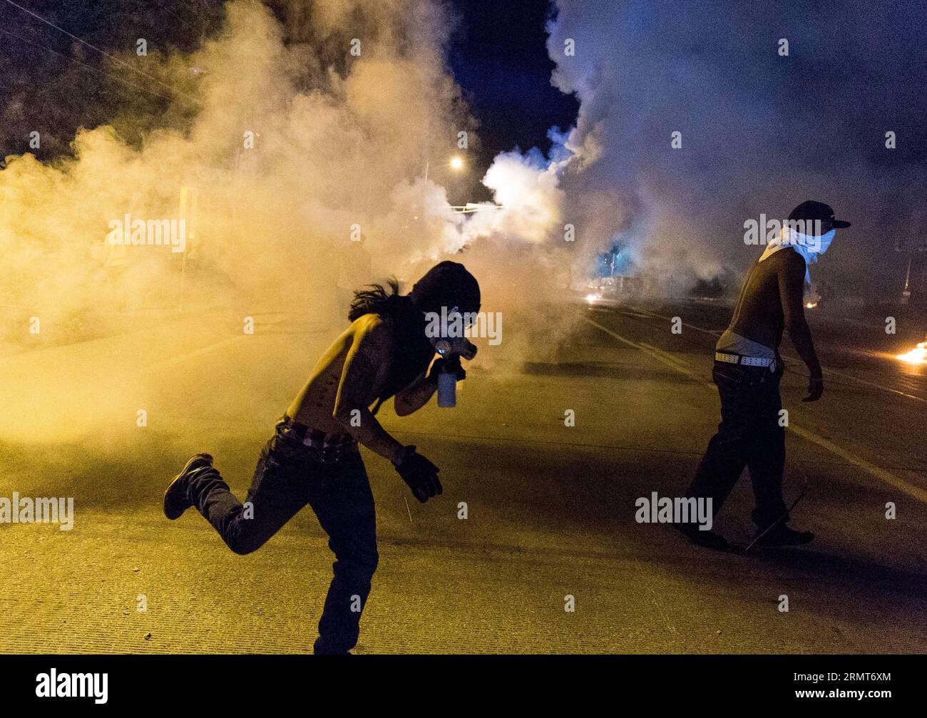 (140819) -- FERGUSON, Aug. 19, 2014 -- A protestor runs from the teargas smoke from the canisters fired by the police during the protests against police killing of Michael Brown in Ferguson, Missouri, the United States.18-year-old African American Michael Brown was shot dead by police in Ferguson, sparking continuous protests in the town where most of the population is black. ) US-MISSOURI-FERGUSON-PROTEST-CLASH ShenxTing PUBLICATIONxNOTxINxCHN   Ferguson Aug 19 2014 a protestor runs from The  Smoke from The canisters FIRED by The Police during The Protest against Police Killing of Michael Bro Stock Photo