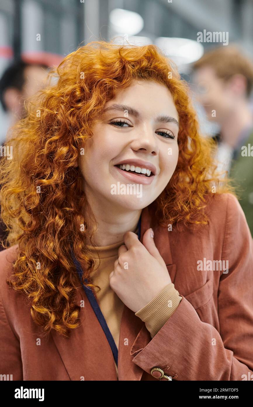 professional headshot of overjoyed redhead businesswoman looking at camera near blurred colleagues Stock Photo